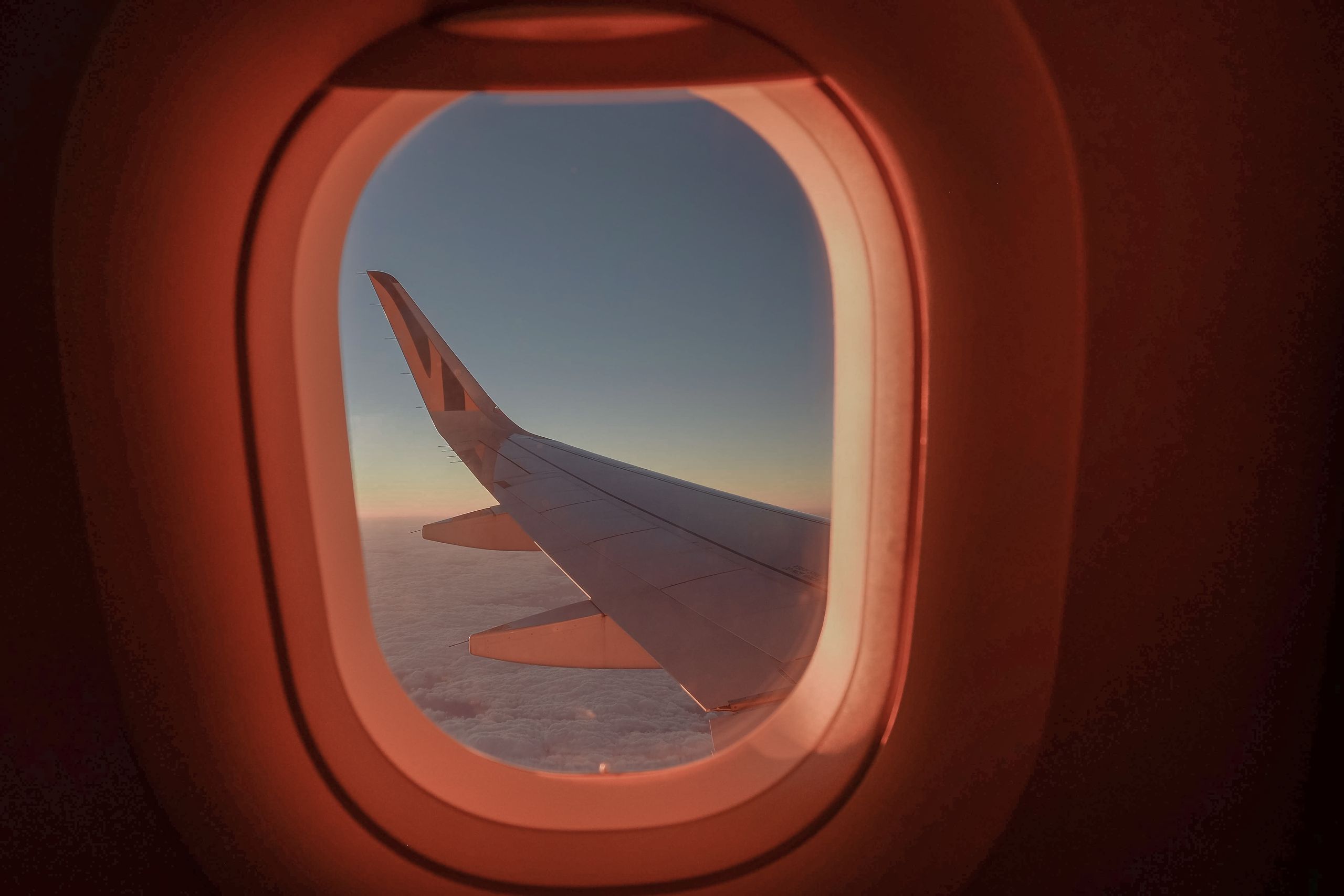 A serene view from an airplane window featuring a wing against a colorful sunset sky, evoking a sense of travel and exploration.