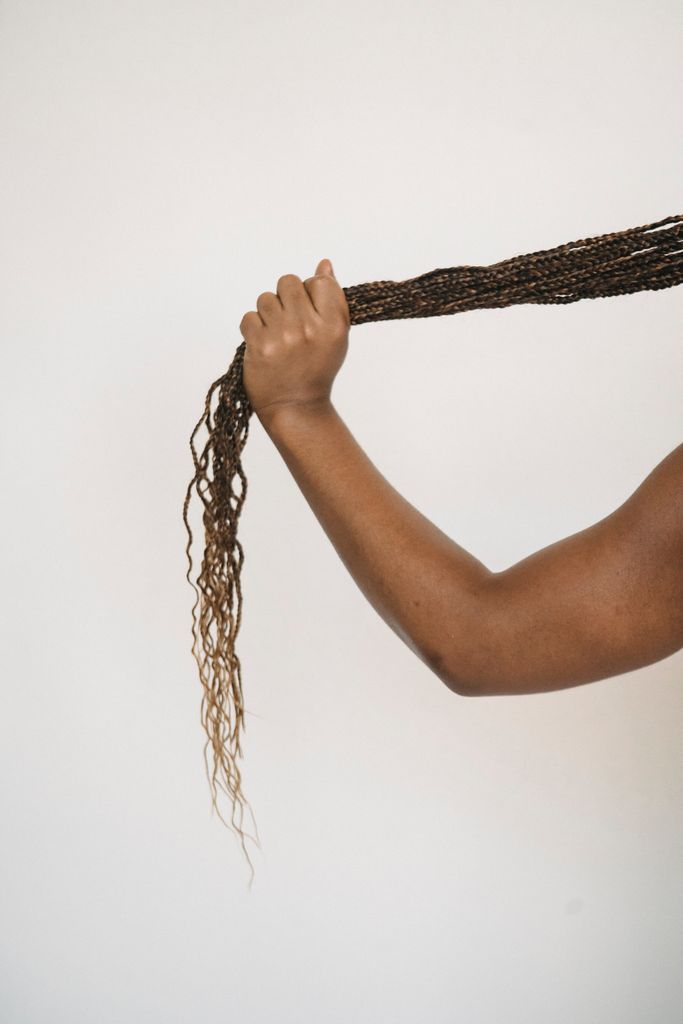Back view unrecognizable ethnic person holding long ponytail of dark African braids against white wall