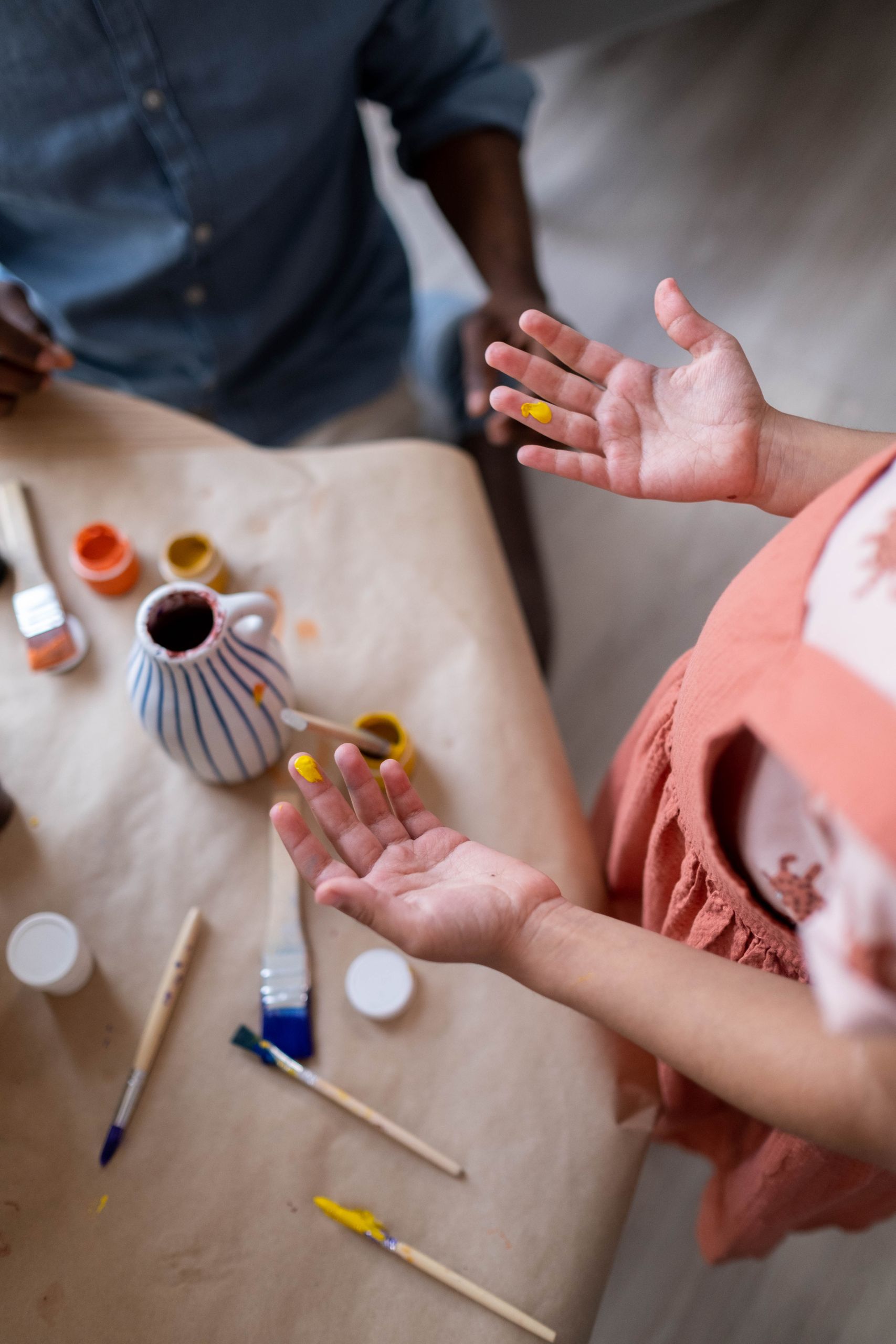 Close-up of hands with paint, engaging in a vibrant art session with brushes and supplies.