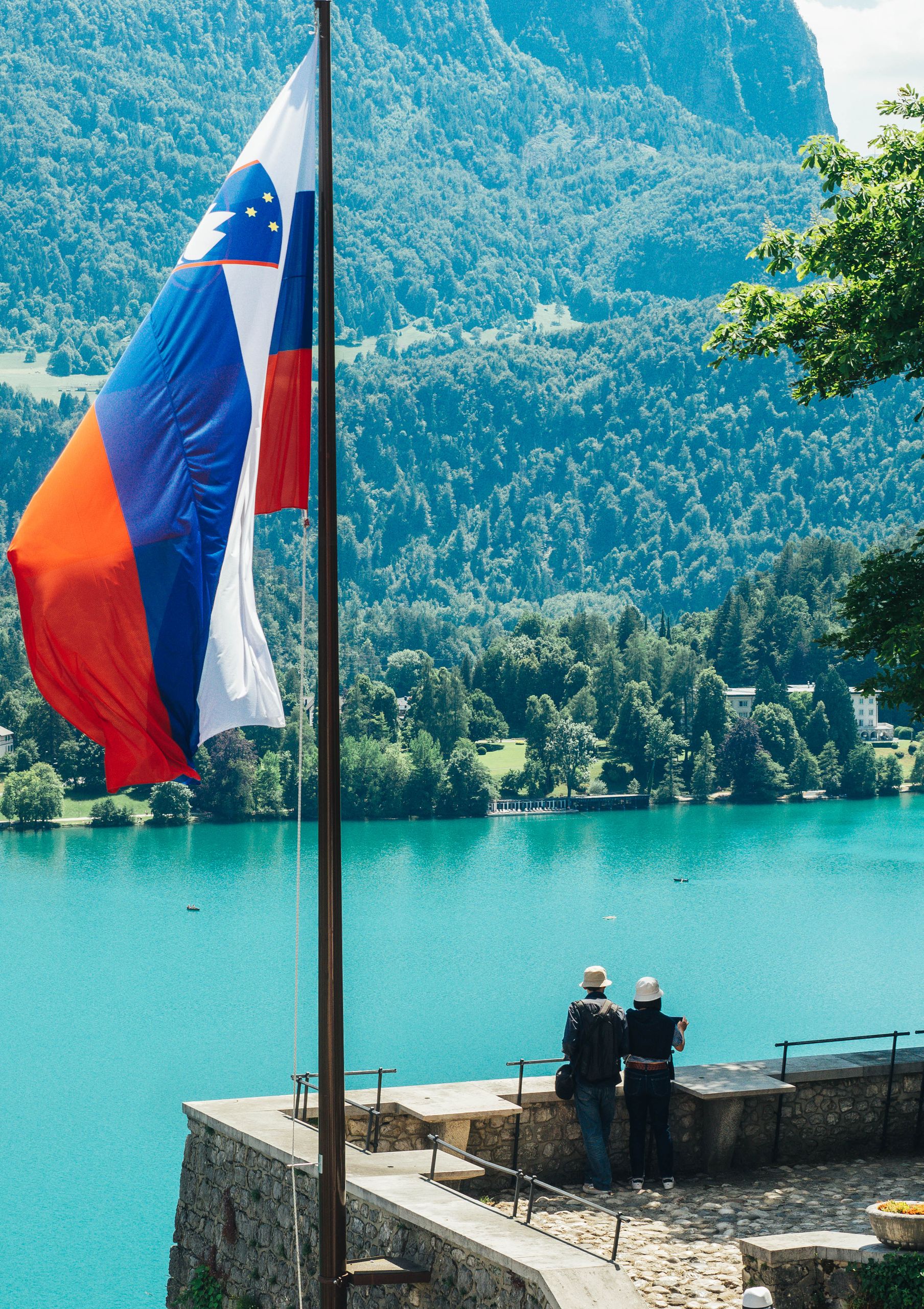Serene Lake Bled view featuring Slovenian flag and lush mountains. Perfect for travel inspiration.