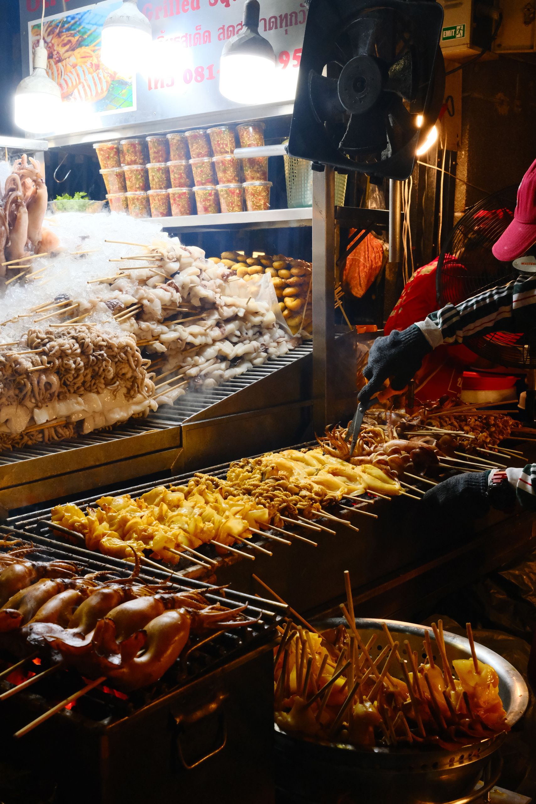 Street vendor grilling seafood and meat skewers at a bustling night market.