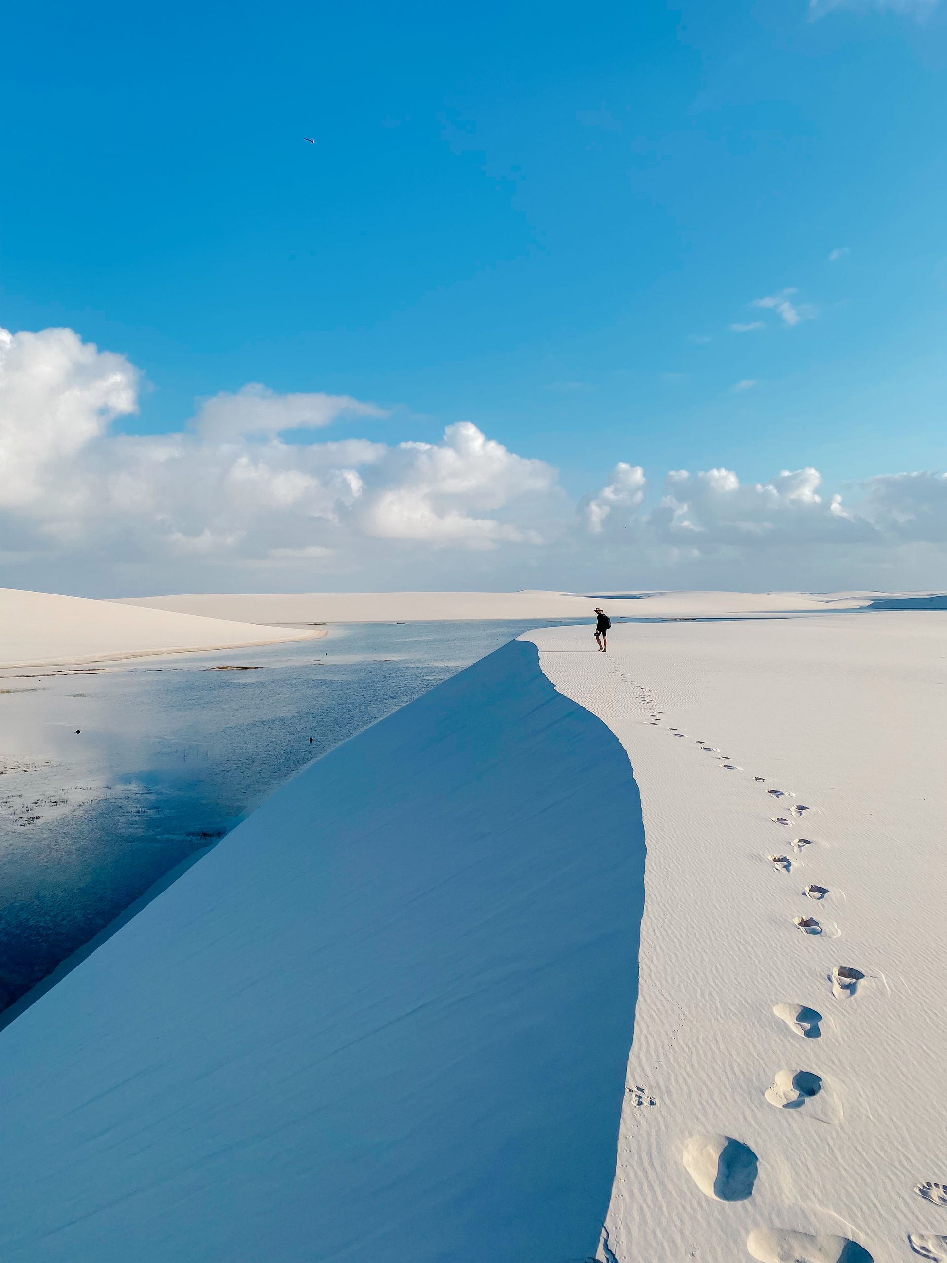 A lone trekker walks along the dunes of Lençóis Maranhenses with a beautiful sky in the background.