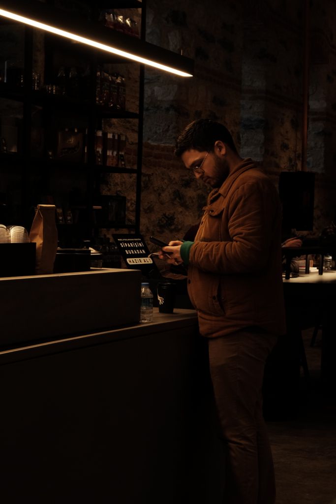 A man stands at a coffee shop counter in Istanbul, using his smartphone during a quiet night.