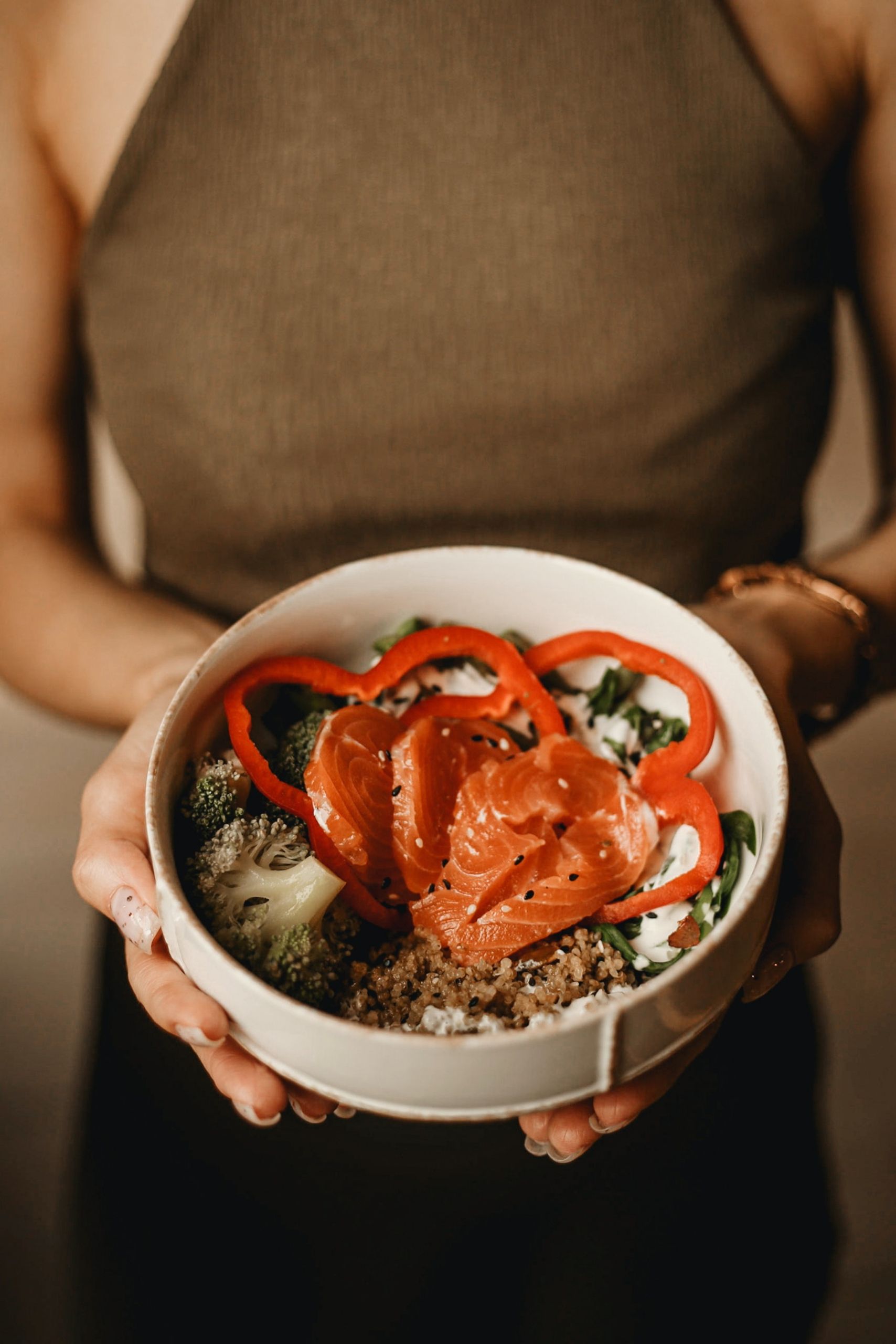 A nutritious bowl of salmon and vegetables held by a person, showcasing vibrant food photography.
