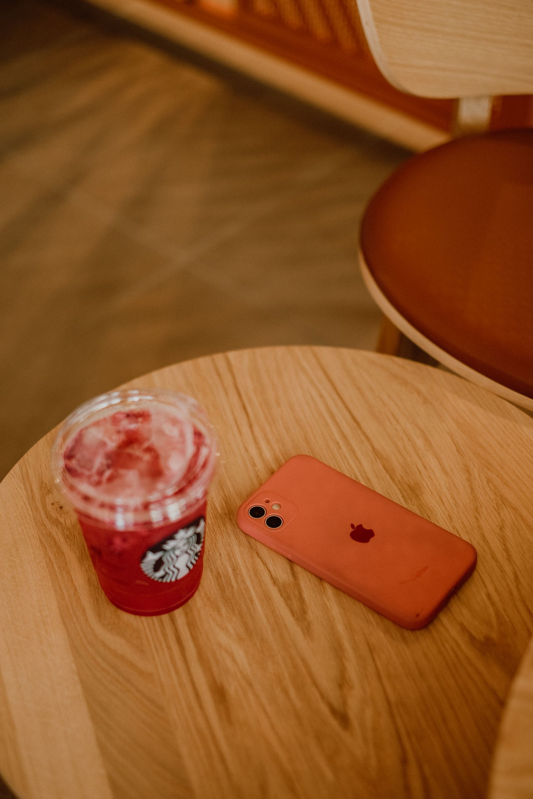 A refreshing iced beverage in a disposable cup next to a smartphone on a wooden table, captured indoors.