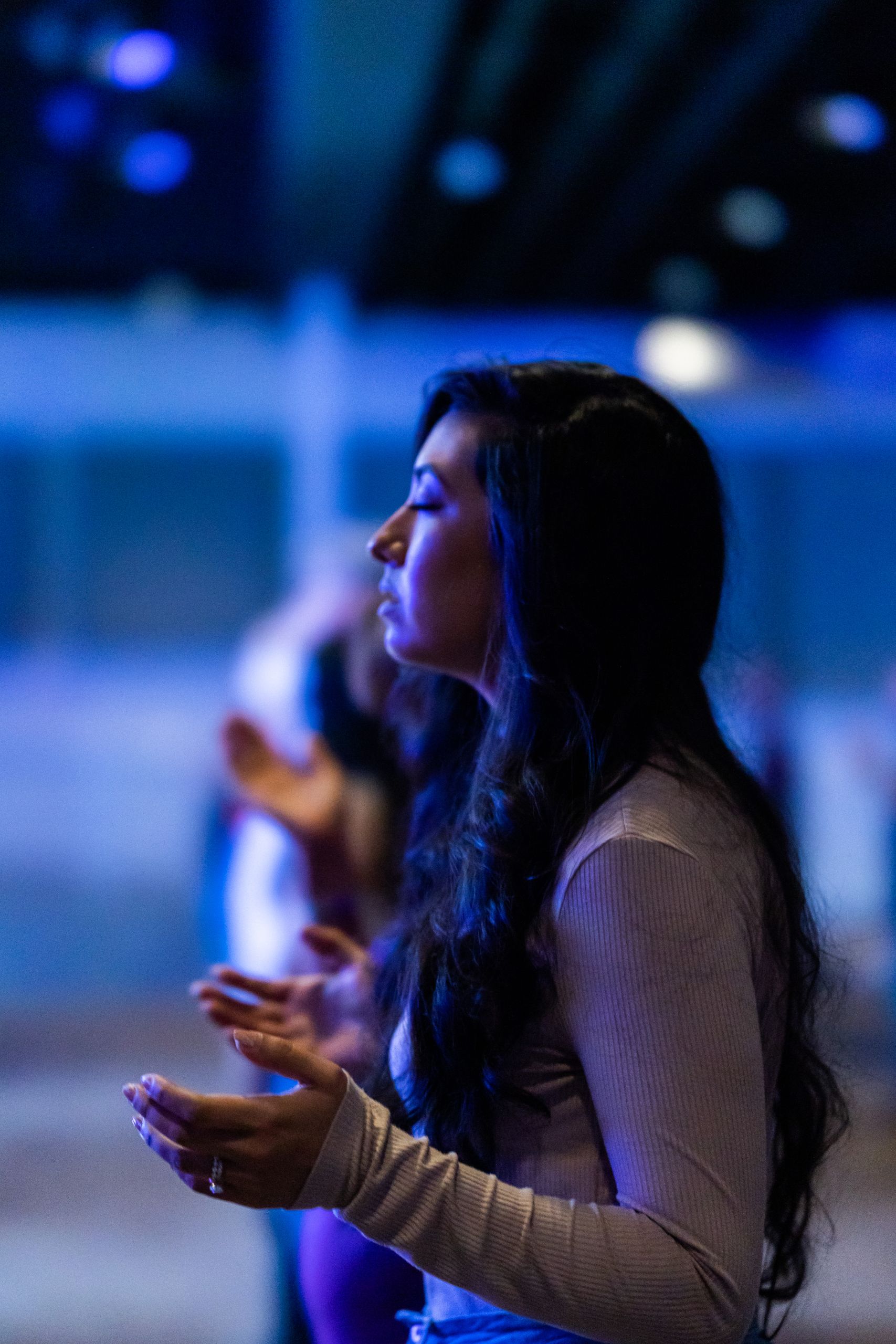 A woman in prayer during a peaceful indoor nighttime service, expressing faith and reflection.