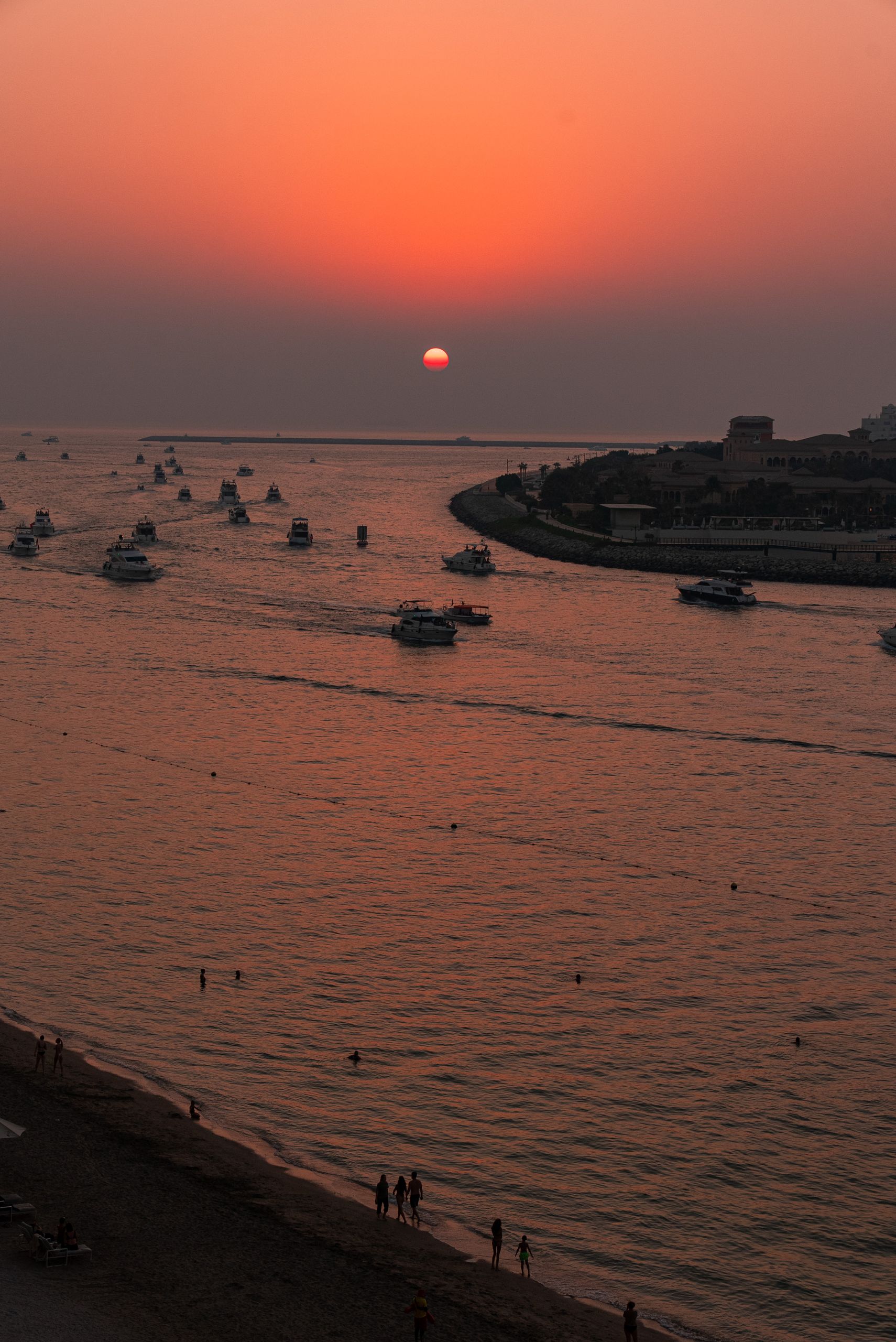 Boats sail at sunset, casting reflections on the calm sea, creating a peaceful seascape.