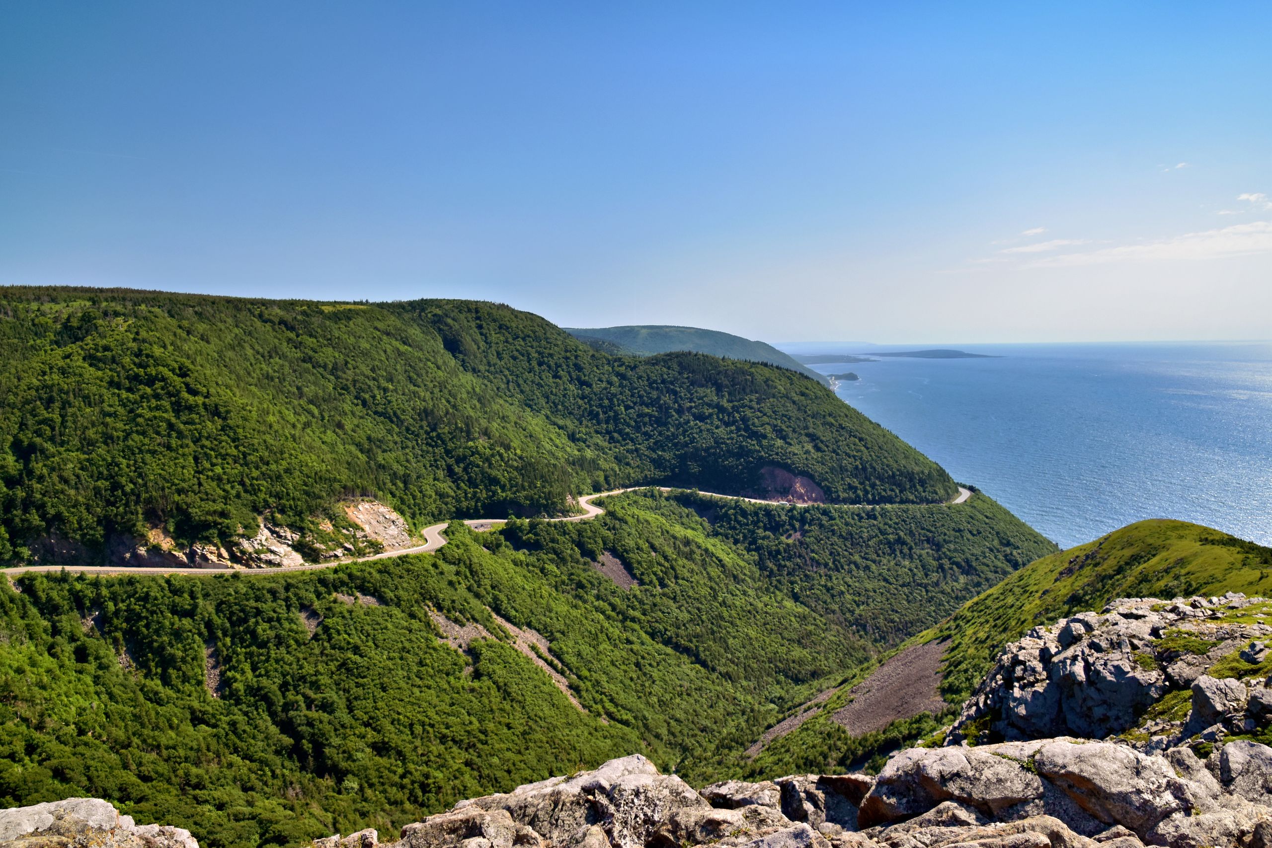 Breathtaking view of the Cabot Trail winding through lush hills and coastal cliffs in Nova Scotia.