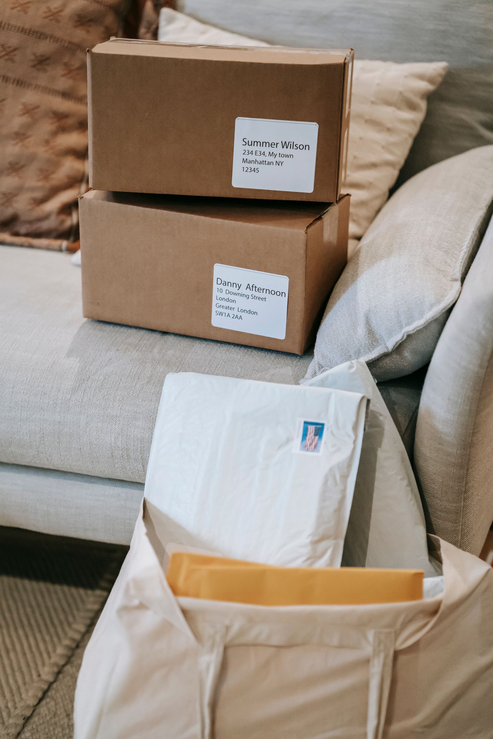 From above of delivered cardboard boxes placed on sofa near letters in envelopes in fabric bag in apartment