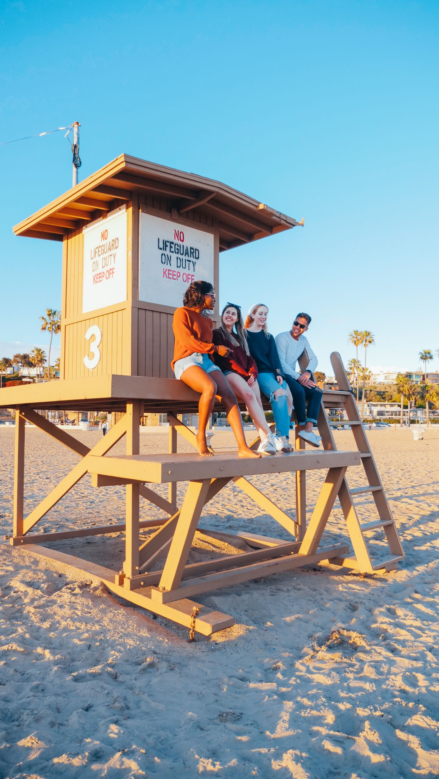 Group of friends sitting on a lifeguard tower at the beach during sunset, enjoying togetherness.