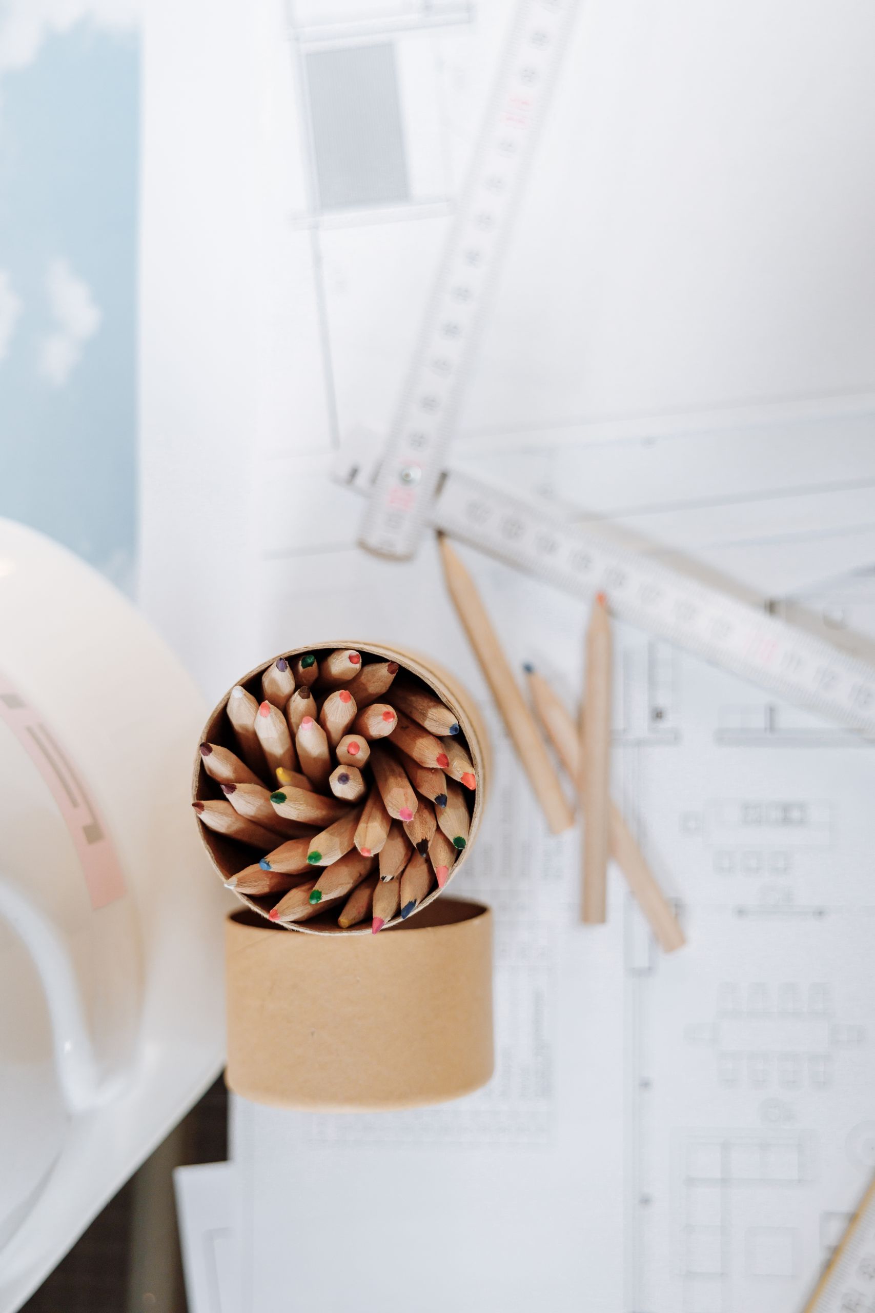 Overhead shot of a creative workspace featuring colored pencils, drafting plans, and measuring tools on a desk.