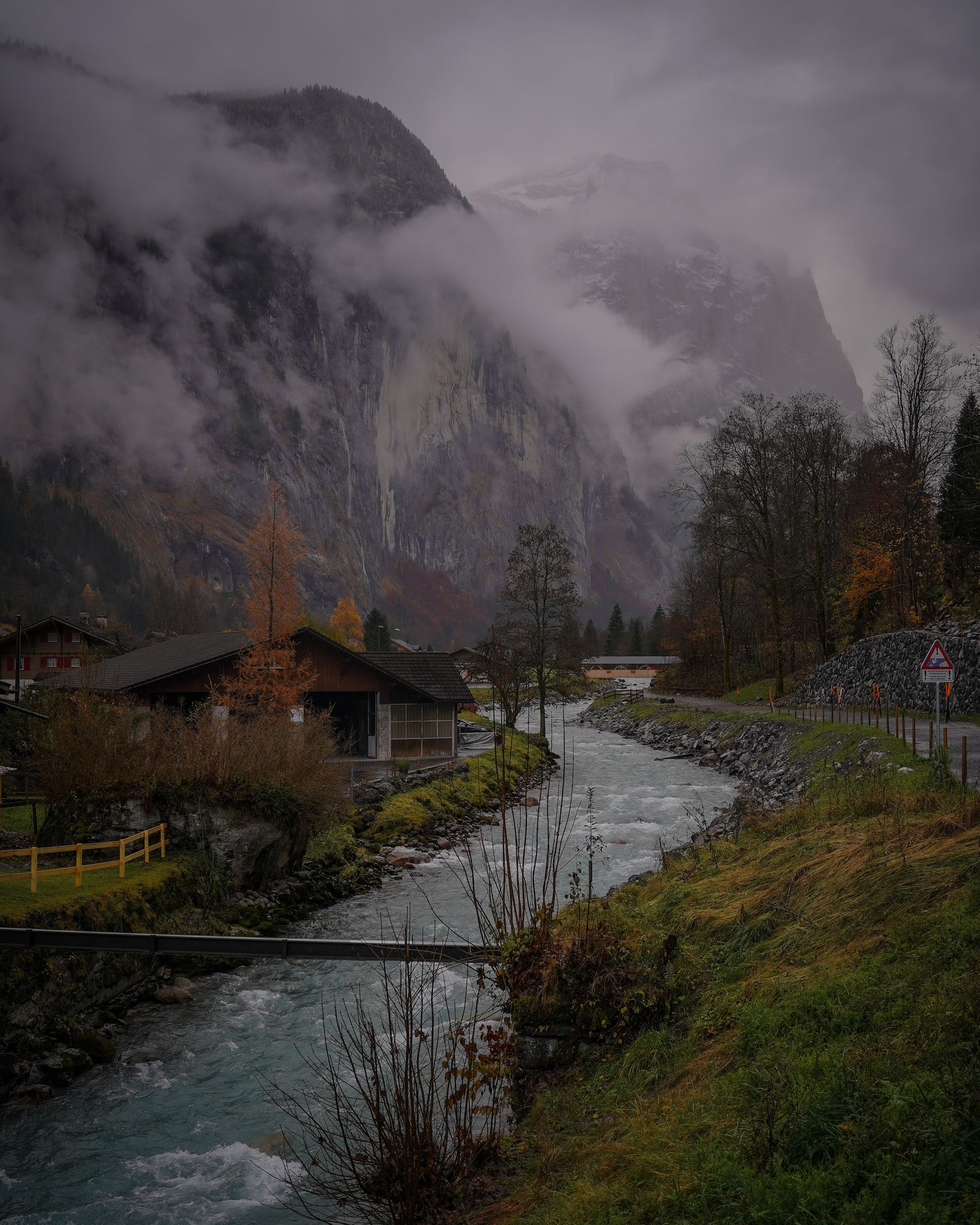 Picturesque autumn landscape of a Swiss village with a river and foggy Alps.