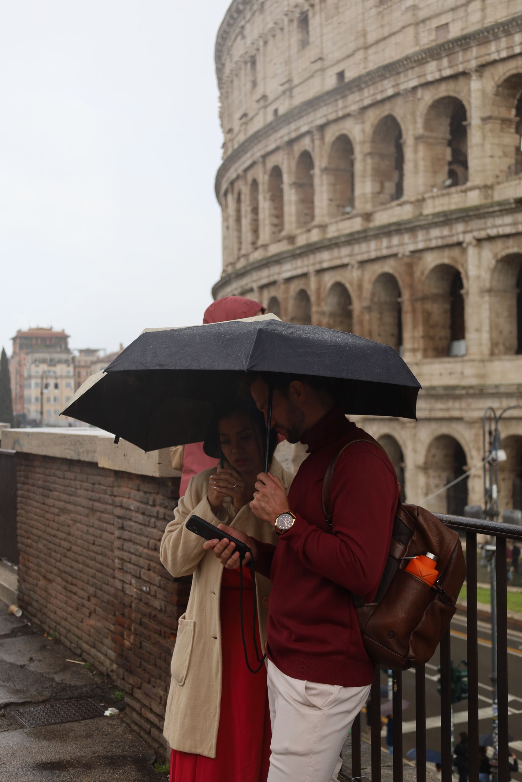 Romantic scene at Colosseum with couple sharing an umbrella on a rainy day.