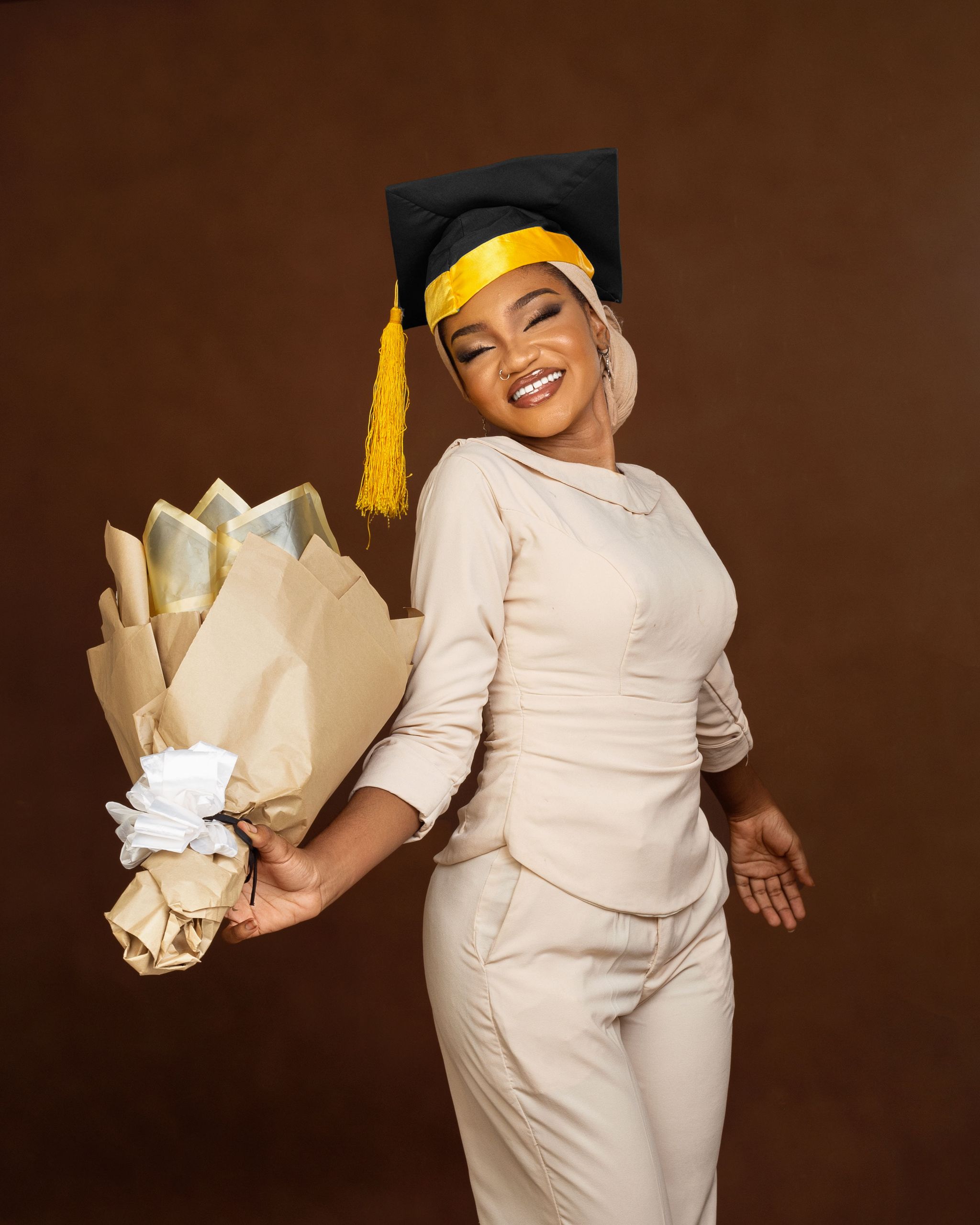 Smiling young graduate celebrating with a bouquet against a brown background.
