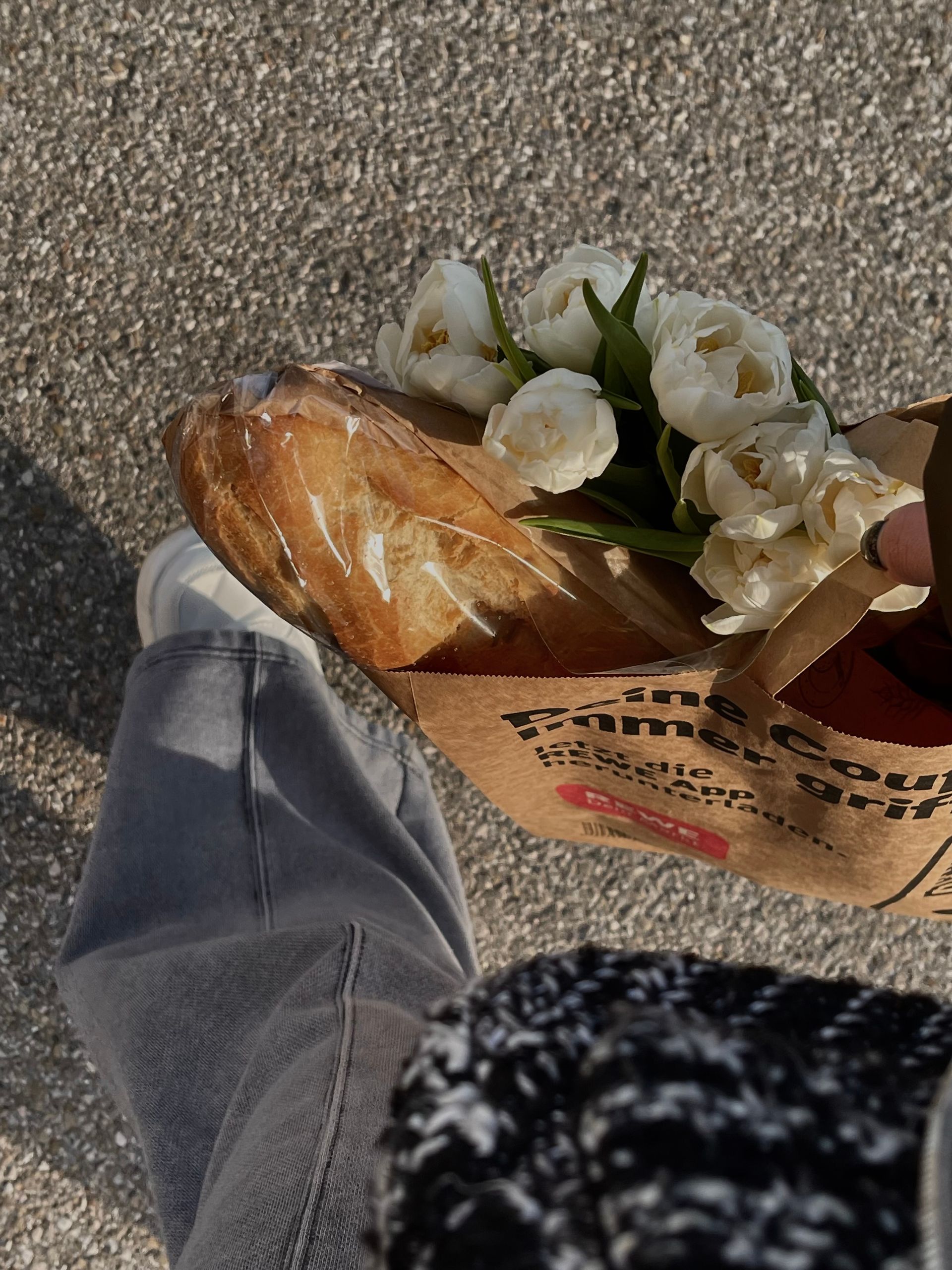 Top view of casual street shopping with paper bag, tulips, and baguette in spring sunlight.