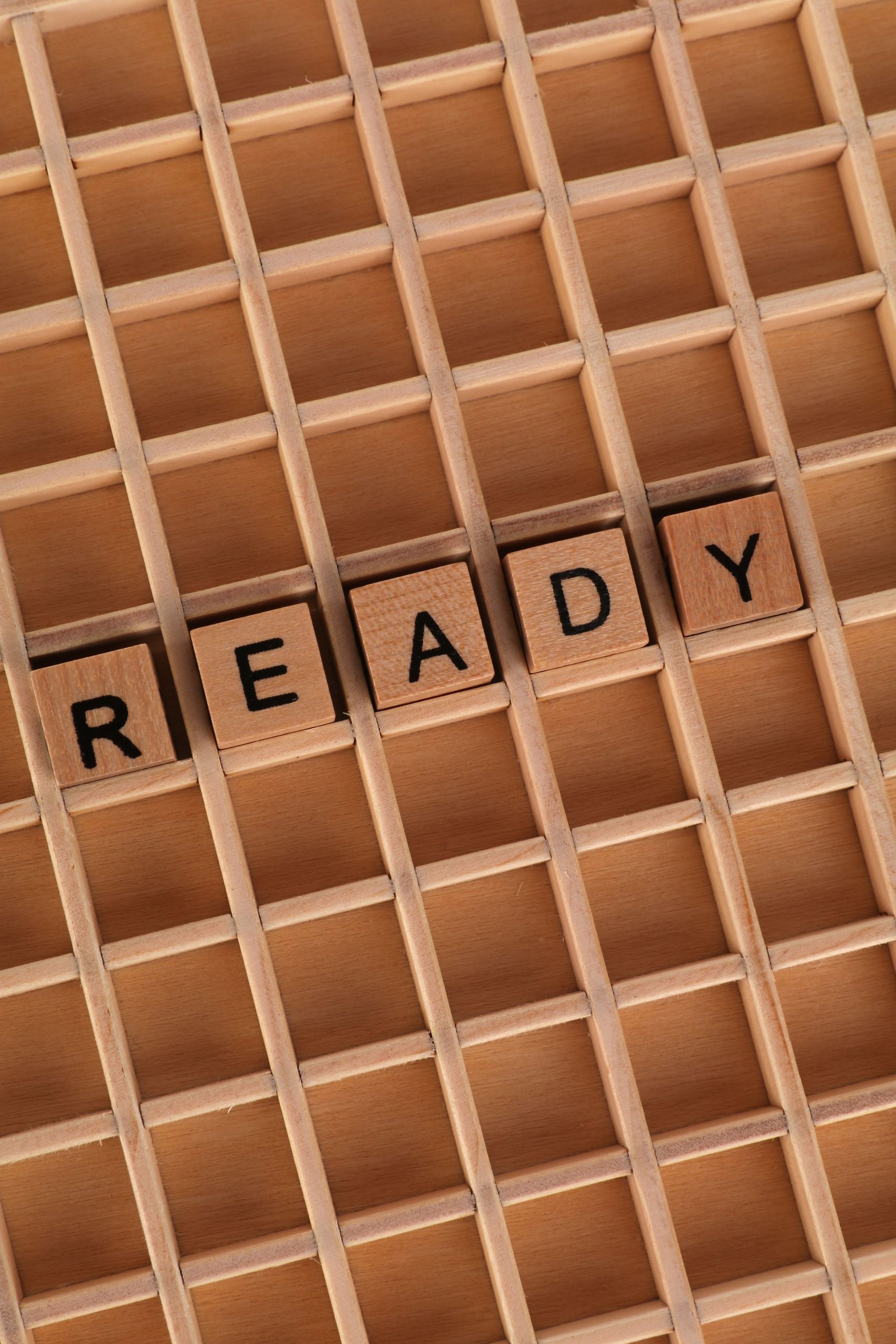 Wooden Scrabble tiles spelling 'READY' on a grid background. Perfect for motivational themes.