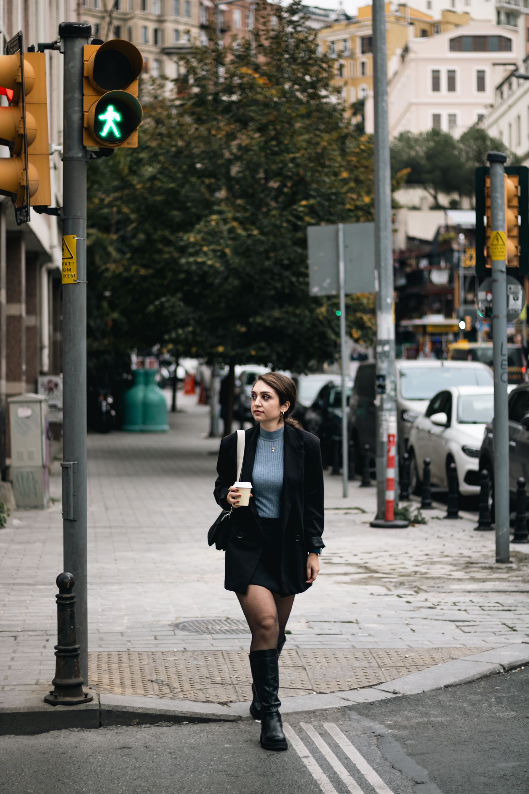 Young woman crossing street with coffee in city setting, capturing everyday urban life.