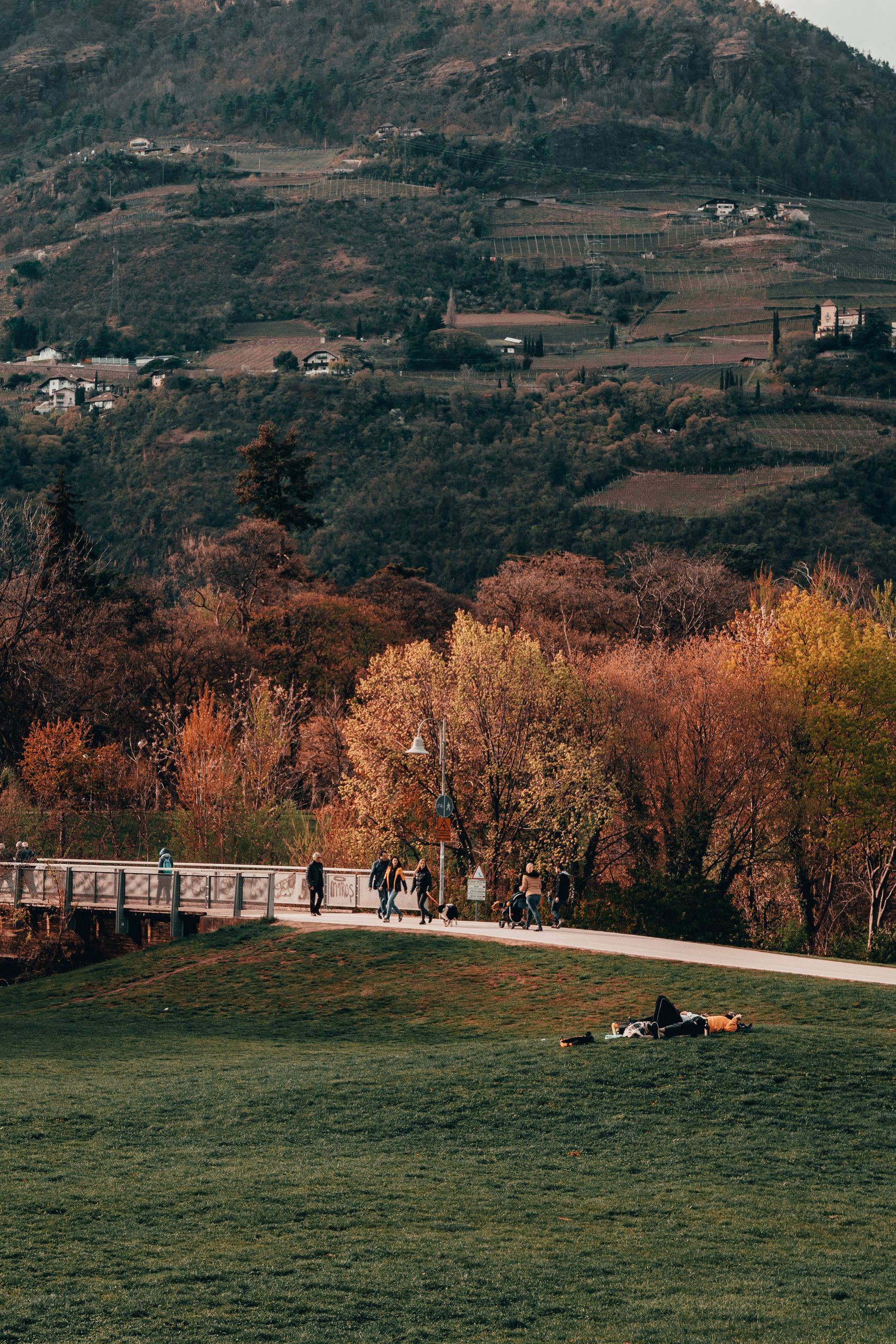 Autumn park scene with people walking along a bridge and vibrant fall foliage.
