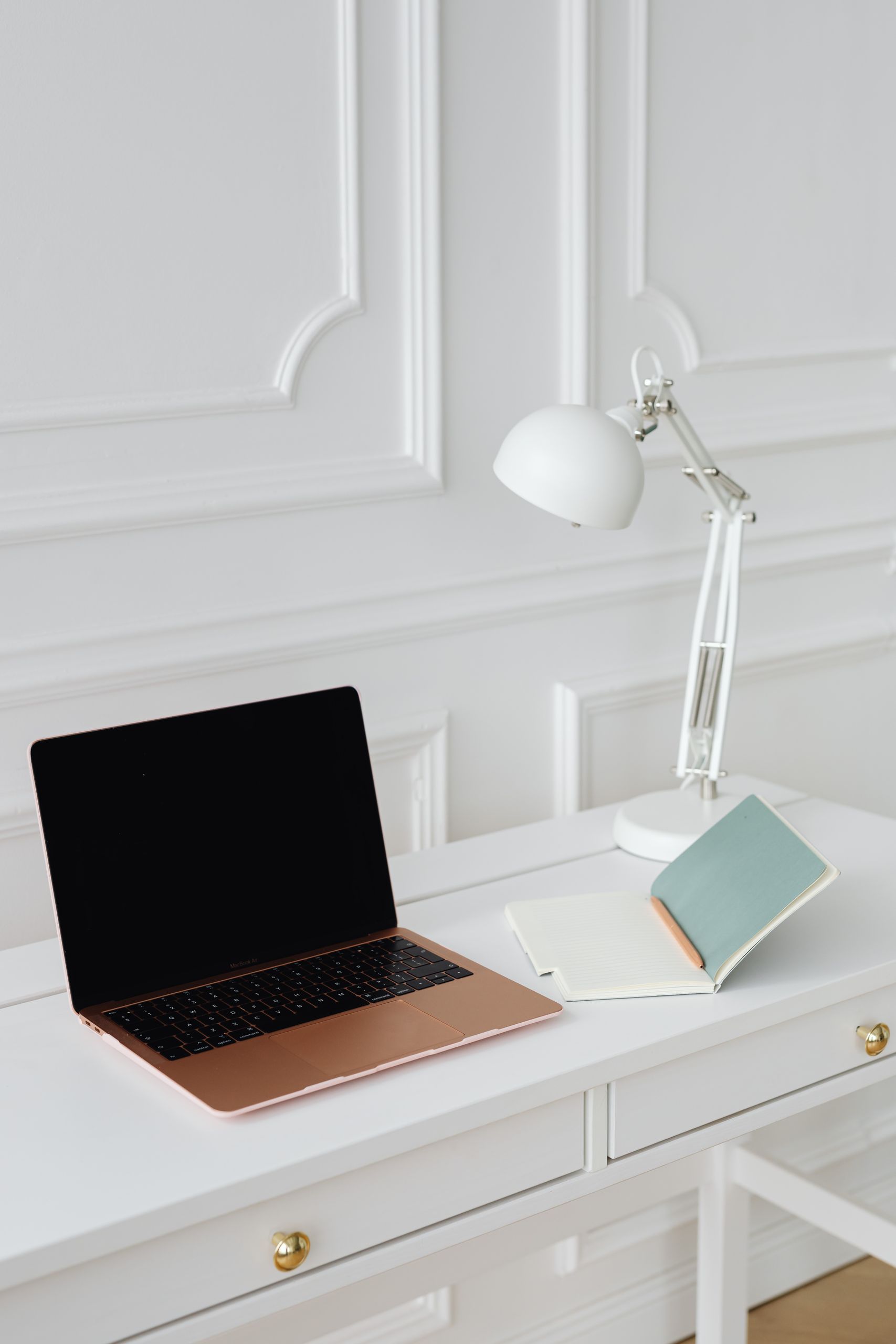 Clean and modern office desk with a laptop, desk lamp, and notebooks in a minimalist setting.