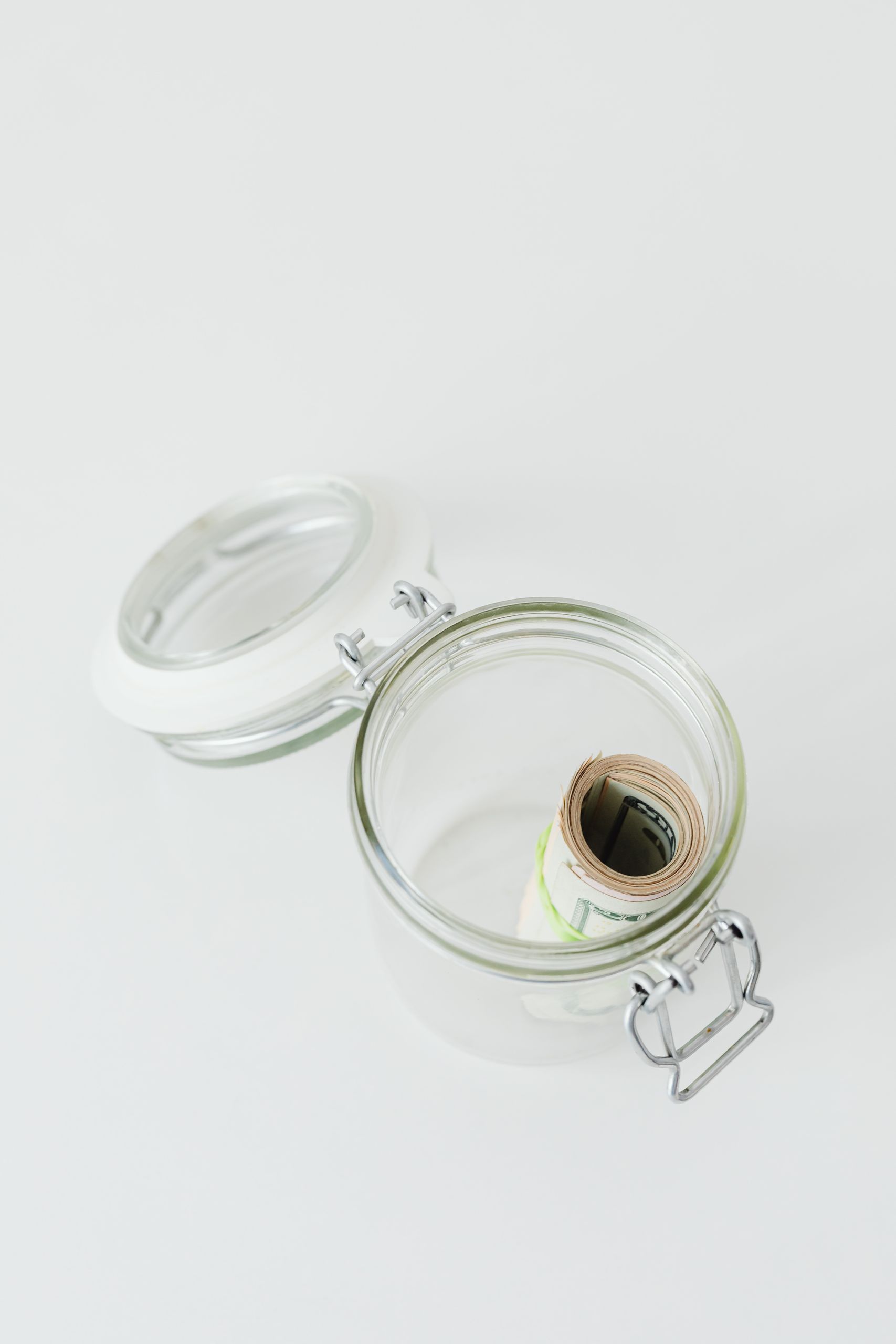 Open glass jar containing rolled paper money, symbolizing savings or finance concept.